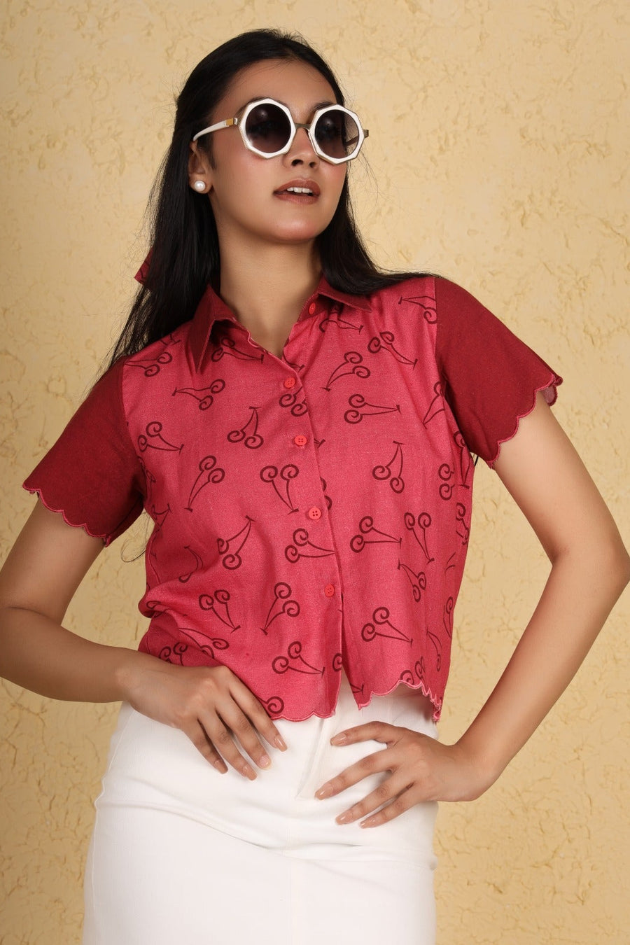 Woman wearing a red patterned blouse and white pants against a beige background